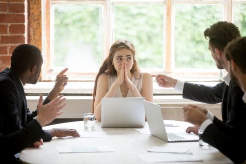 multiple men talking and pointing at a woman in a board room